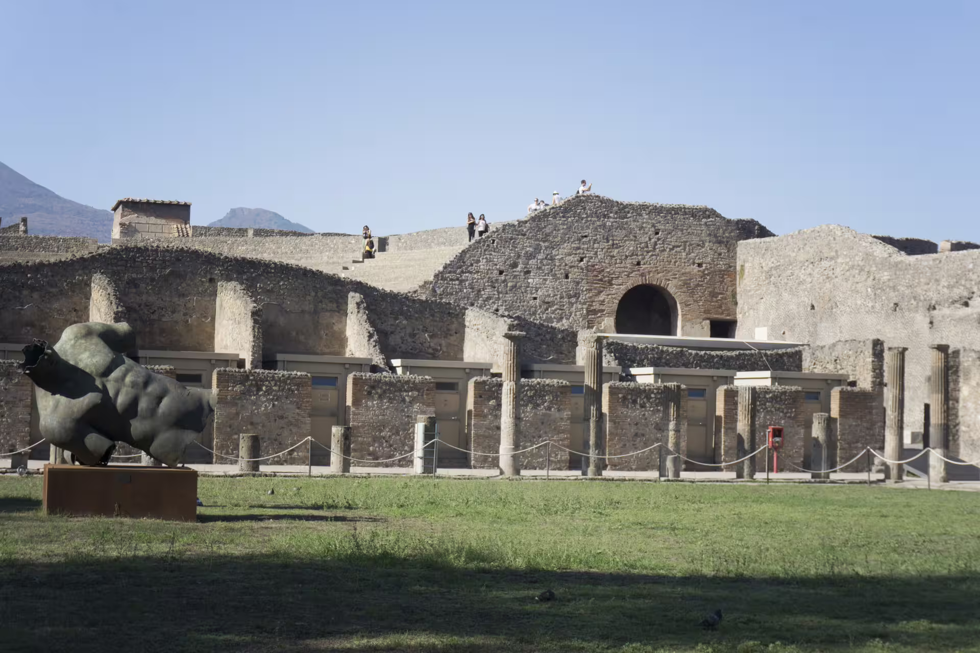 Green lawn, modern sculpture and stone ruins of Pompeii amphitheater explored on a semi private afternoon tour from Rome