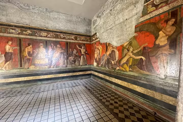 Vibrant ancient frescoes adorn the walls of a Pompeii villa, showcasing Roman art on a guided tour with skip-the-line entry.