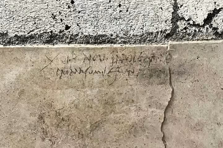 Faded ancient graffiti on a stone wall in Pompeii, offering a glimpse into Roman life on a private guided tour.