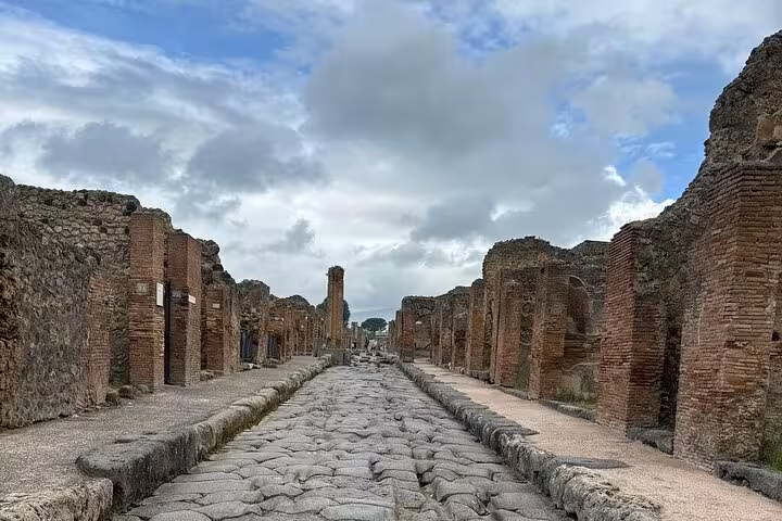 View of a cobblestone street lined with ancient ruins in Pompeii, highlighting historical architecture on Sorrento guided tour.