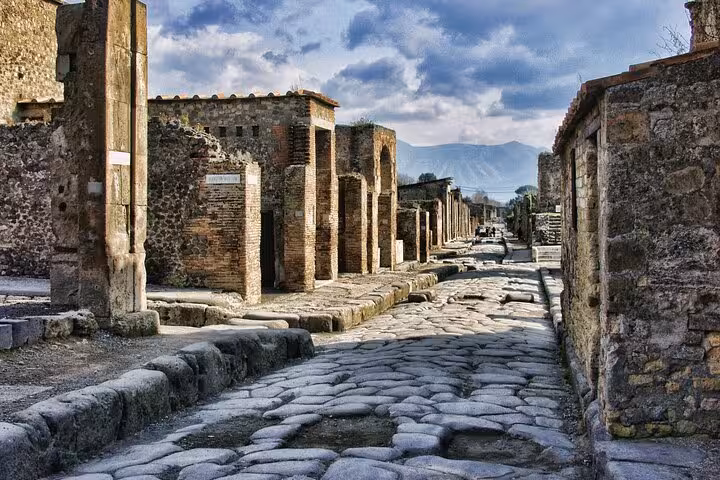 Cobblestone street and ancient ruins of Pompeii with mountains in the background, highlighting historical architecture.
