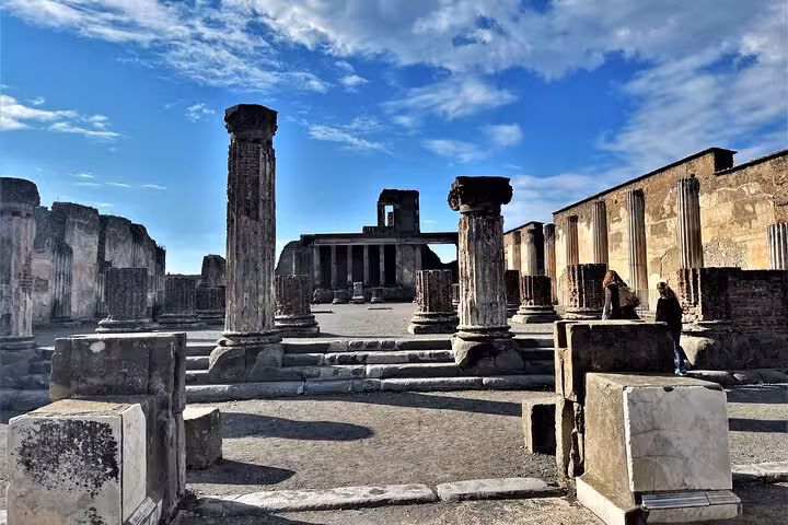 Ancient ruins of Pompeii with towering columns under a blue sky, featured in the Pompeii Guided Tour from Sorrento Coast.