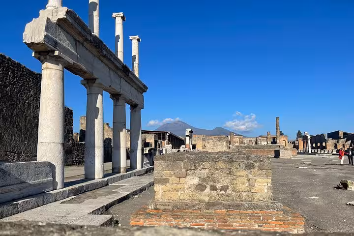 View of Pompeii's ancient ruins with Mount Vesuvius in the distance under a clear blue sky.