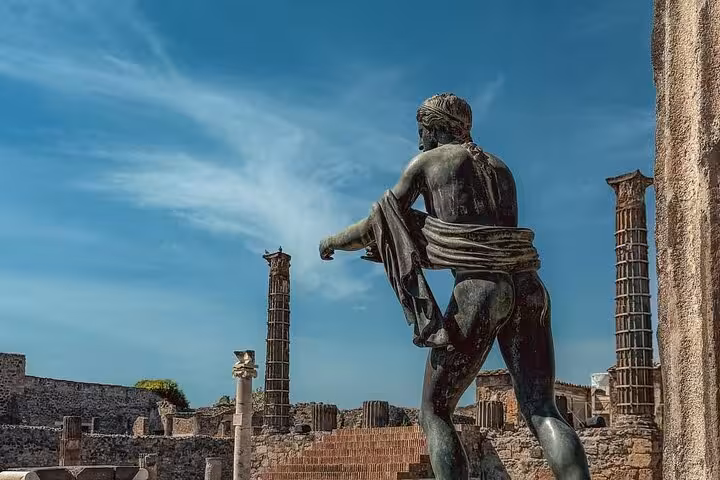 Ancient statue amidst Pompeii ruins with clear skies, showcasing historical architecture and cultural exploration.