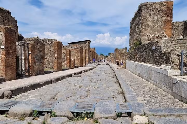 Ancient stone street in Pompeii with ruins and a clear blue sky, ideal for a historical day trip.