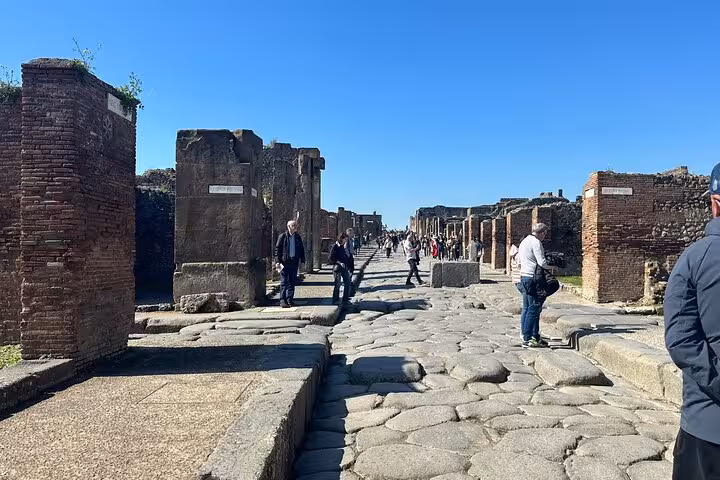 Visitors walk along ancient stone streets in Pompeii, part of the scenic tour from Positano to Mt. Vesuvius.