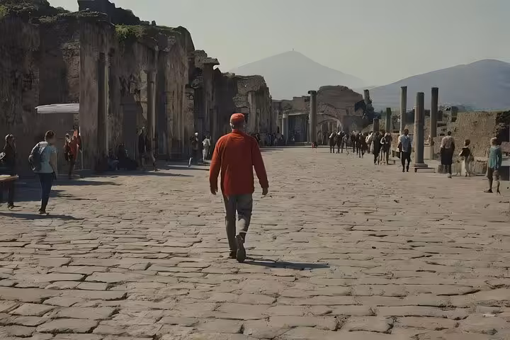 Tourists explore the ancient stone-paved streets of Pompeii with Mt. Vesuvius looming in the background.