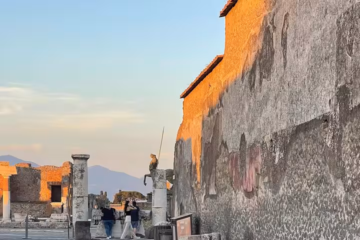 Golden sunset light casts a warm glow on the ancient stone walls and sculptures of Pompeii's historic site.