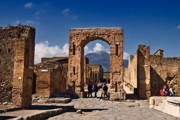 Discover the historic archways of Pompeii's archaeological site with Mount Vesuvius looming in the distance.