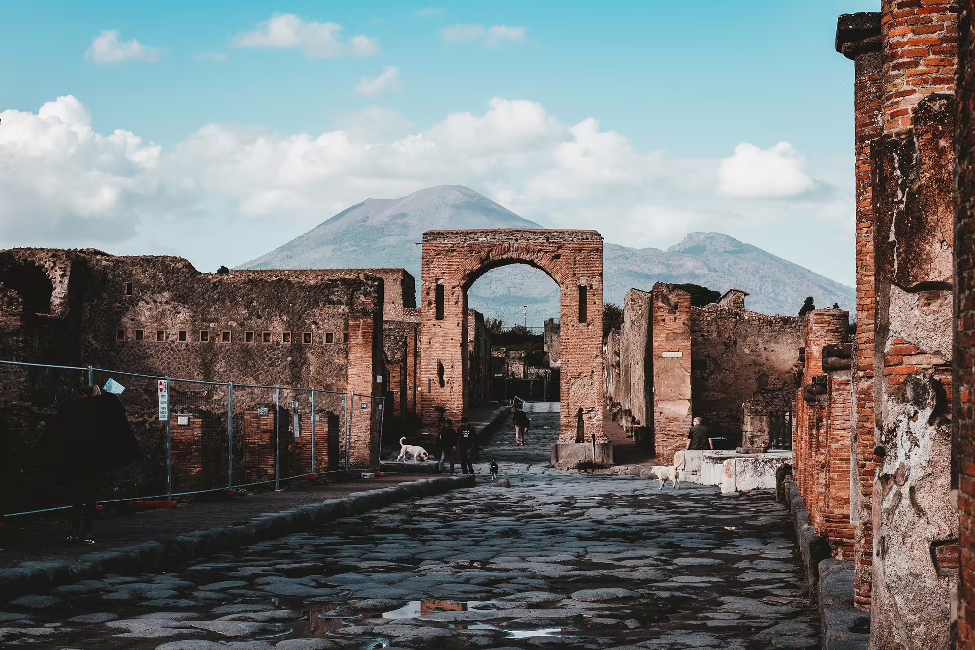 Ancient Pompeii cobblestone road and arch with Mount Vesuvius backdrop on a budget tour from Naples
