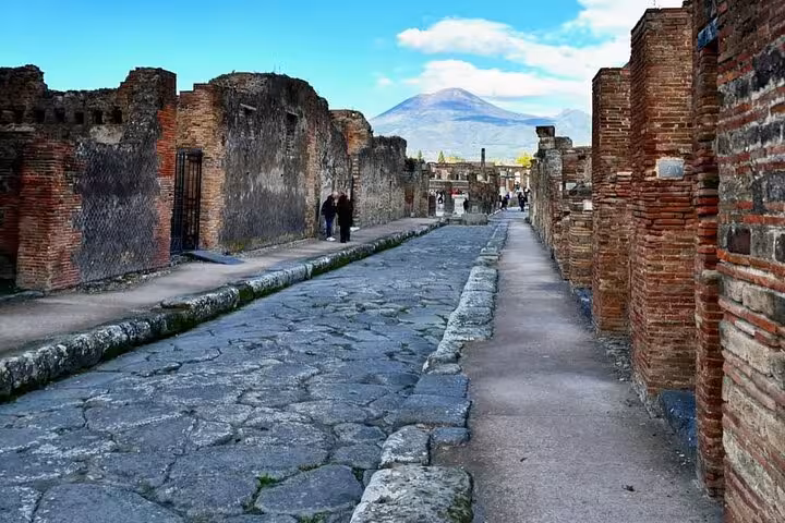 Cobblestone street in ancient Pompeii with Mount Vesuvius in the distance, featured in a guided Sorrento day tour.