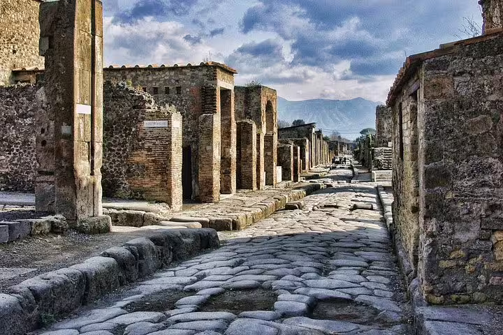 Ancient cobblestone street in Pompeii ruins with Mount Vesuvius view, half-day group tour from Naples