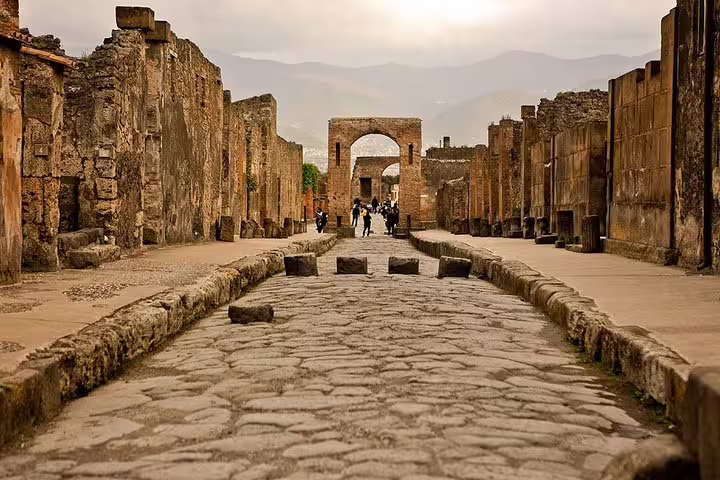 Ancient cobblestone street in Pompeii ruins on low-cost day tour from Naples with Mount Vesuvius views