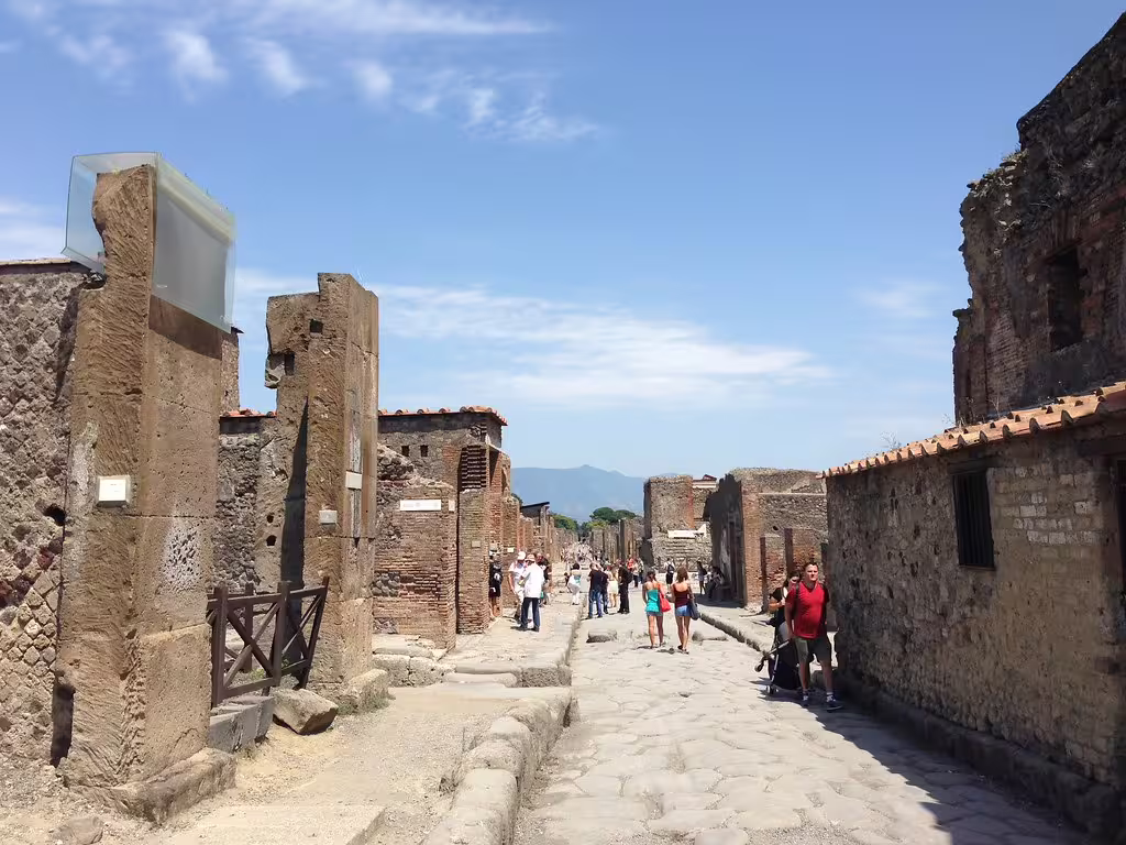 Visitors walking along a sunny cobbled street between preserved ruins during a guided daily tour of ancient Pompeii