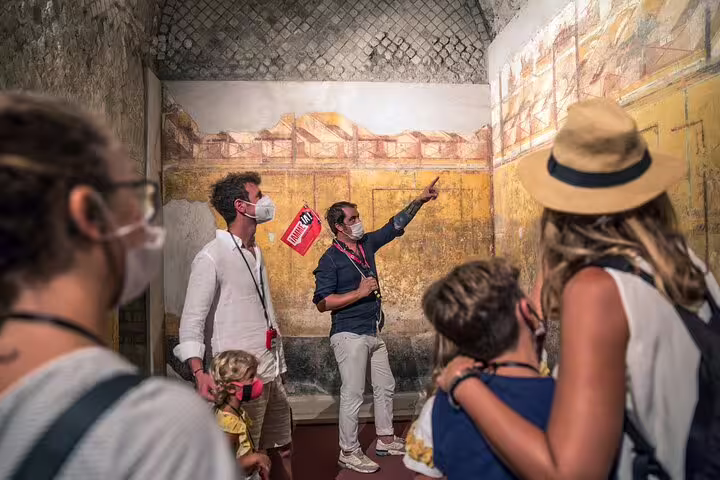 Guide explaining vibrant frescoes to visitors inside Pompeii ruins, highlighting historical art during a Naples day tour.