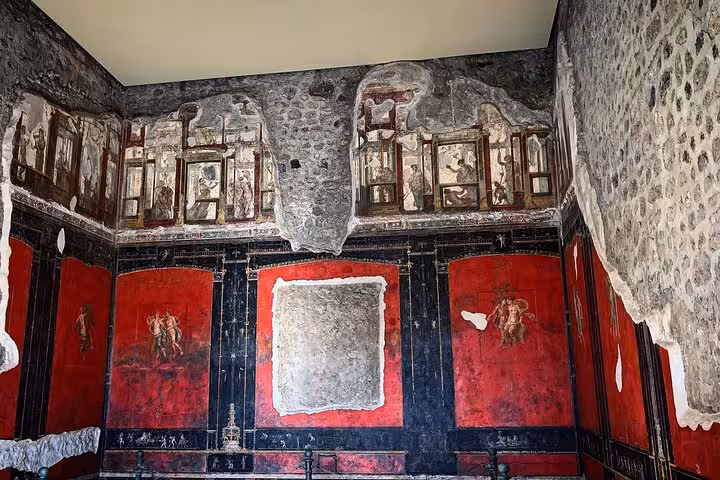 Intricate Pompeii frescoes with vibrant red hues on an ancient wall, part of the Pompeii and Mt. Vesuvius tour.
