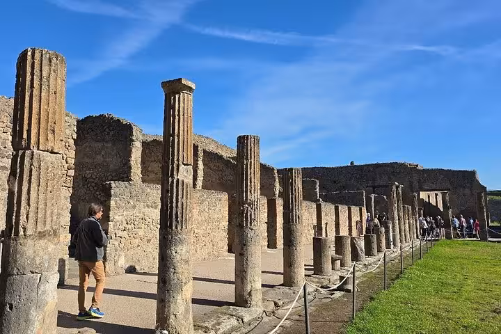Visitors walk among ancient columns in Pompeii during a guided tour with lunch from Sorrento under a clear blue sky.