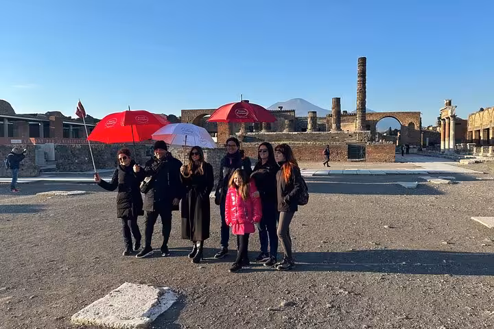 Tour group with umbrellas exploring Pompeii's ancient ruins with Mount Vesuvius in the background on a skip-the-line guided tour.