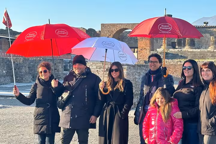 Group of tourists with umbrellas enjoy a sunny guided tour in the ancient ruins of Pompeii from Sorrento Coast.