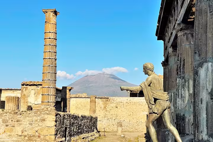 Statue and ancient ruins in Pompeii with Mount Vesuvius in the background, seen on a guided tour from Naples.