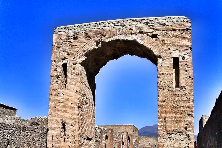Explore ancient Pompeii's iconic stone archway under a clear blue sky on a guided tour from Sorrento with lunch.