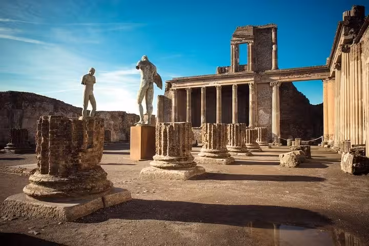 Ancient statues and columns in the ruins of Pompeii under a clear blue sky on an 8-hour Hercolaneum, Pompeii, Sorrento tour.