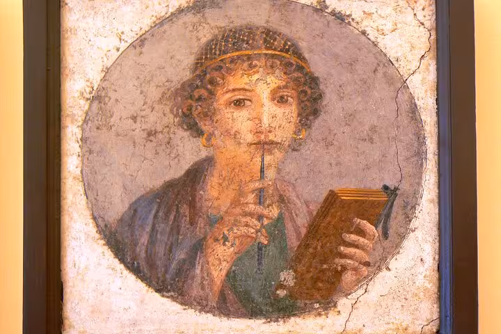 Ancient fresco of a woman holding a stylus and wax tablet, part of the Pompeii and Herculaneum tour package.