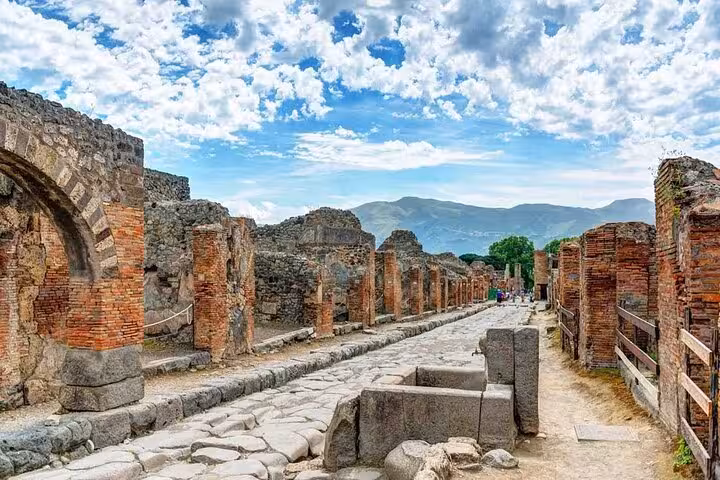 Ancient stone street and ruins of Pompeii under a bright blue sky, showcasing the historical architecture.