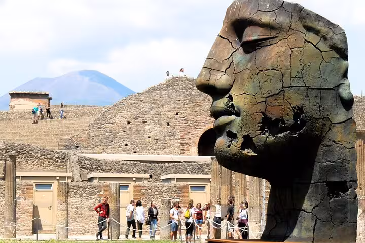 Tourists exploring ancient ruins in Pompeii with a striking bronze sculpture and Mount Vesuvius in the background.