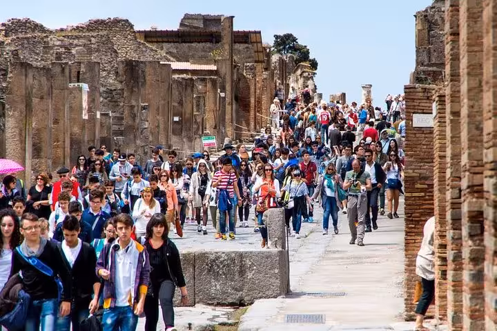 Crowds of tourists exploring the ancient ruins of Pompeii on a sunny day, experiencing the historical site.