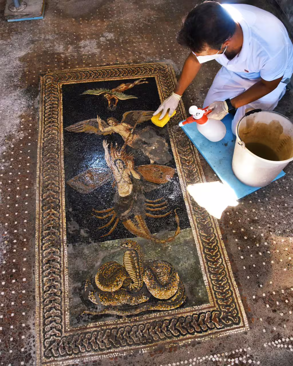 Conservator cleaning ancient Pompeii mosaic on affordable Pompeii and Mount Vesuvius tour from Naples