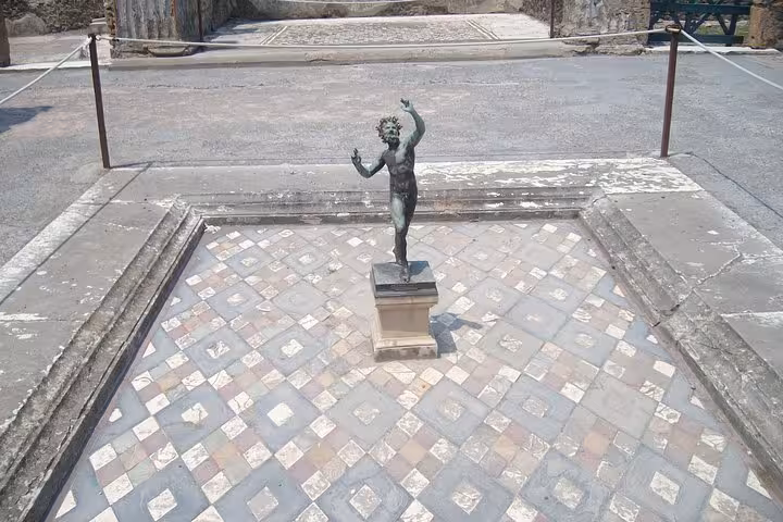 Bronze statue of a dancing faun on a tiled floor at Pompeii, a highlight of the Pompeii & Mount Vesuvius tour.