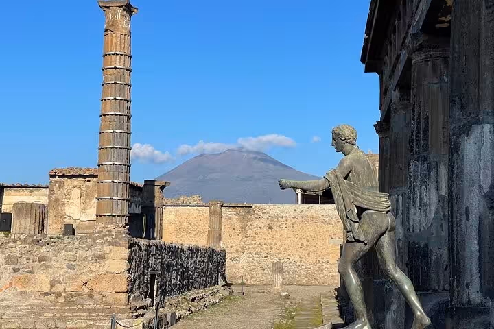 View of Mount Vesuvius from Pompeii ruins, with ancient statues and columns, included in Positano tour package.