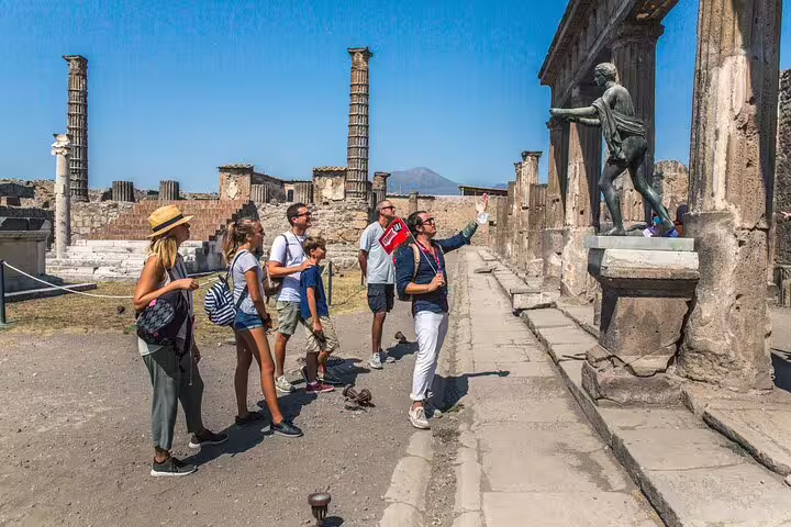 Visitors explore Pompeii with a guide pointing at a historical statue on a Skip The Line tour from Sorrento.