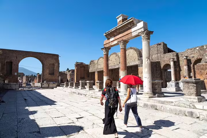 Small group on a private Pompeii tour walking past Roman columns and temples with expert guide under a bright blue sky