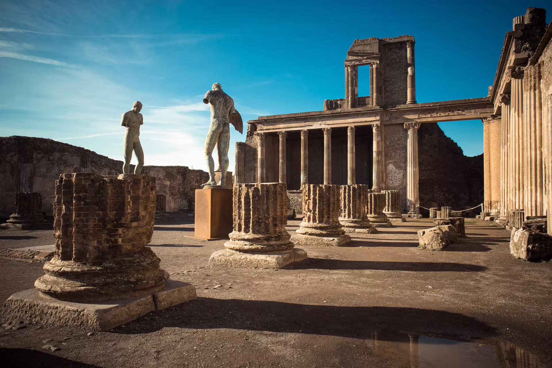 Pompeii ruins with statues and ancient columns, highlight of a half-day group tour from Naples