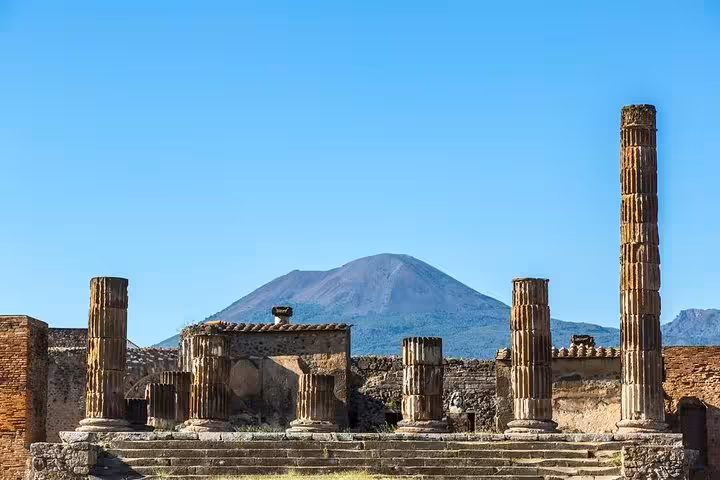 Ancient ruins of Pompeii with Mount Vesuvius looming in the background under a clear blue sky.