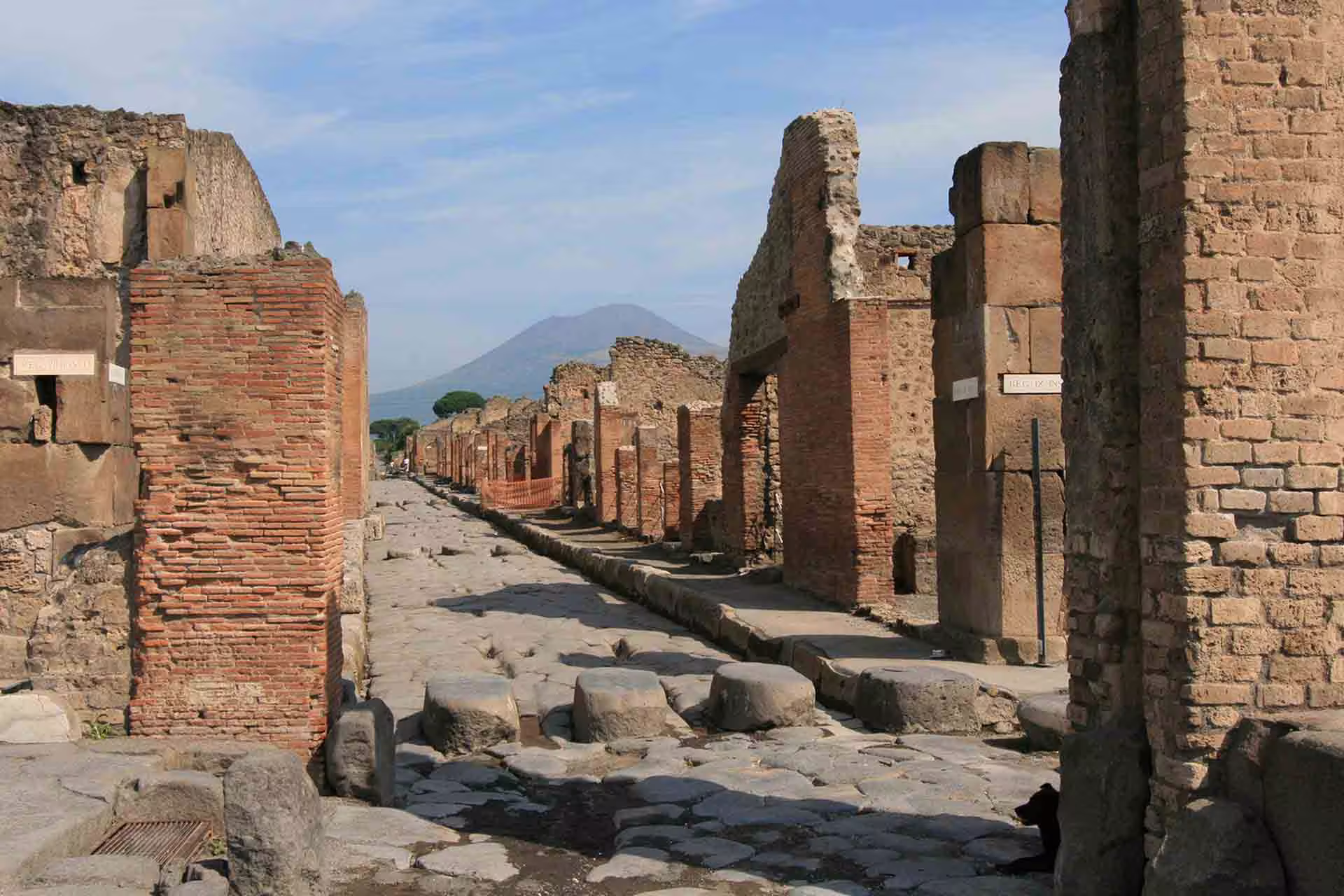 Pompeii ruins street with Mount Vesuvius view, low cost day trip from Naples to the ancient city