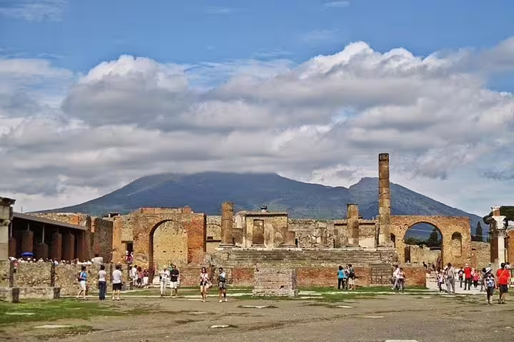 Visitors explore ancient Pompeii ruins with Mount Vesuvius in the background on a full-day private tour from Sorrento