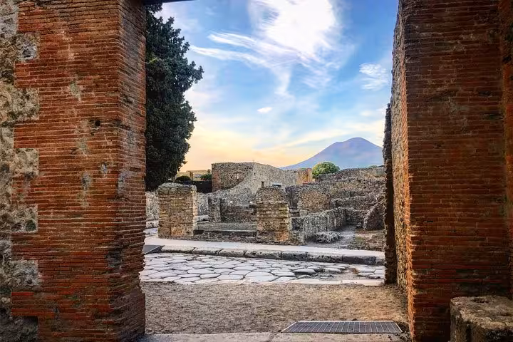 Scenic view of Pompeii ruins framed by ancient walls with Mount Vesuvius in the background under a vibrant sky.