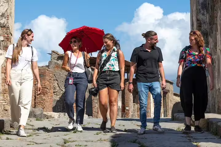 Small group with local guide walking through ancient Pompeii streets under the sun, enjoying an immersive archaeological tour