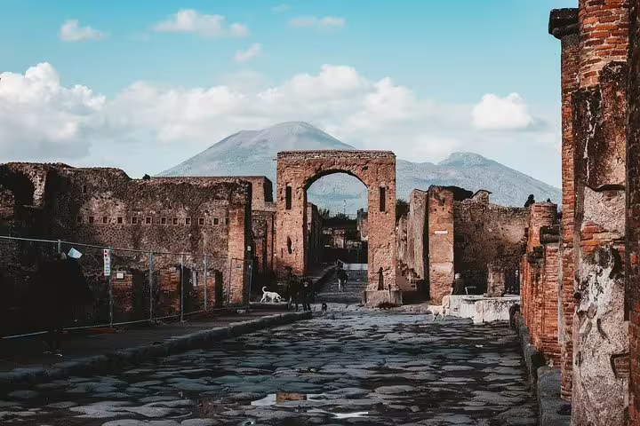 Ancient Pompeii street with archway and Mount Vesuvius view on low cost day trip from Naples