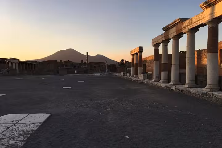 Sunset view of Pompeii ruins with Mount Vesuvius in the background, highlighting ancient columns and architecture.
