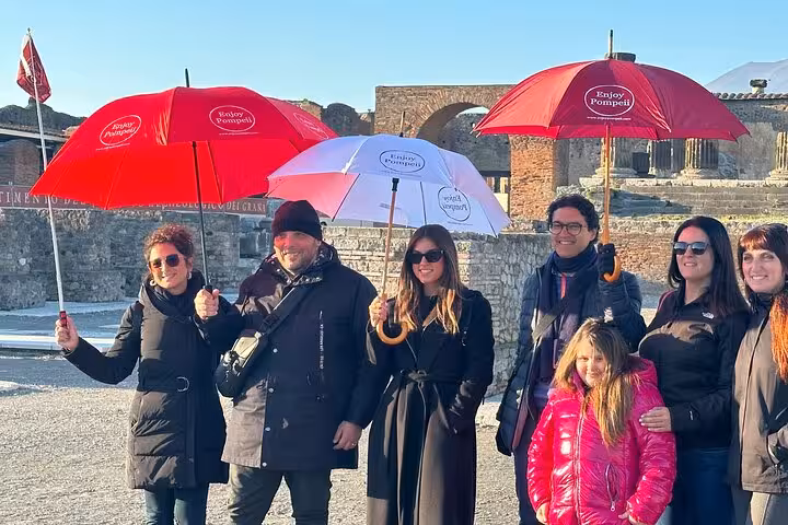 Tourists with umbrellas exploring ancient ruins in Pompeii on a sunny day, highlighting the charm of this historic site.