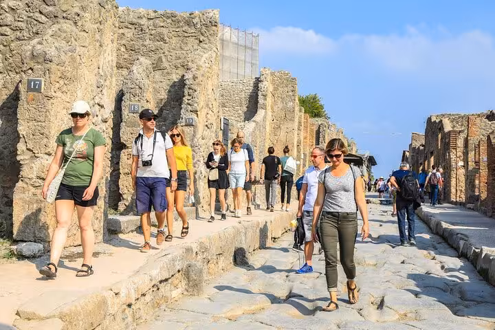 Visitors walking through the ancient streets of Pompeii, experiencing the historical ruins on a guided tour.