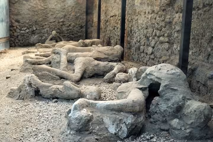 Plaster casts of Pompeii victims preserved in volcanic ash, displayed along ancient stone walls