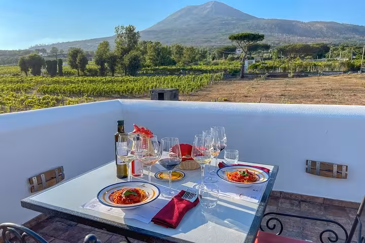 Alfresco dining setup with wine and pasta overlooking lush vineyards and Mount Vesuvius in the background.