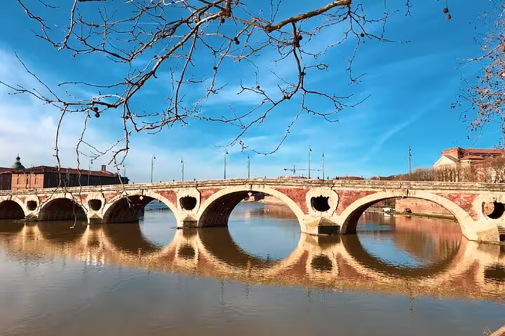 Pont Neuf bridge with stone arches reflecting in the Garonne River in Toulouse, France under blue sky