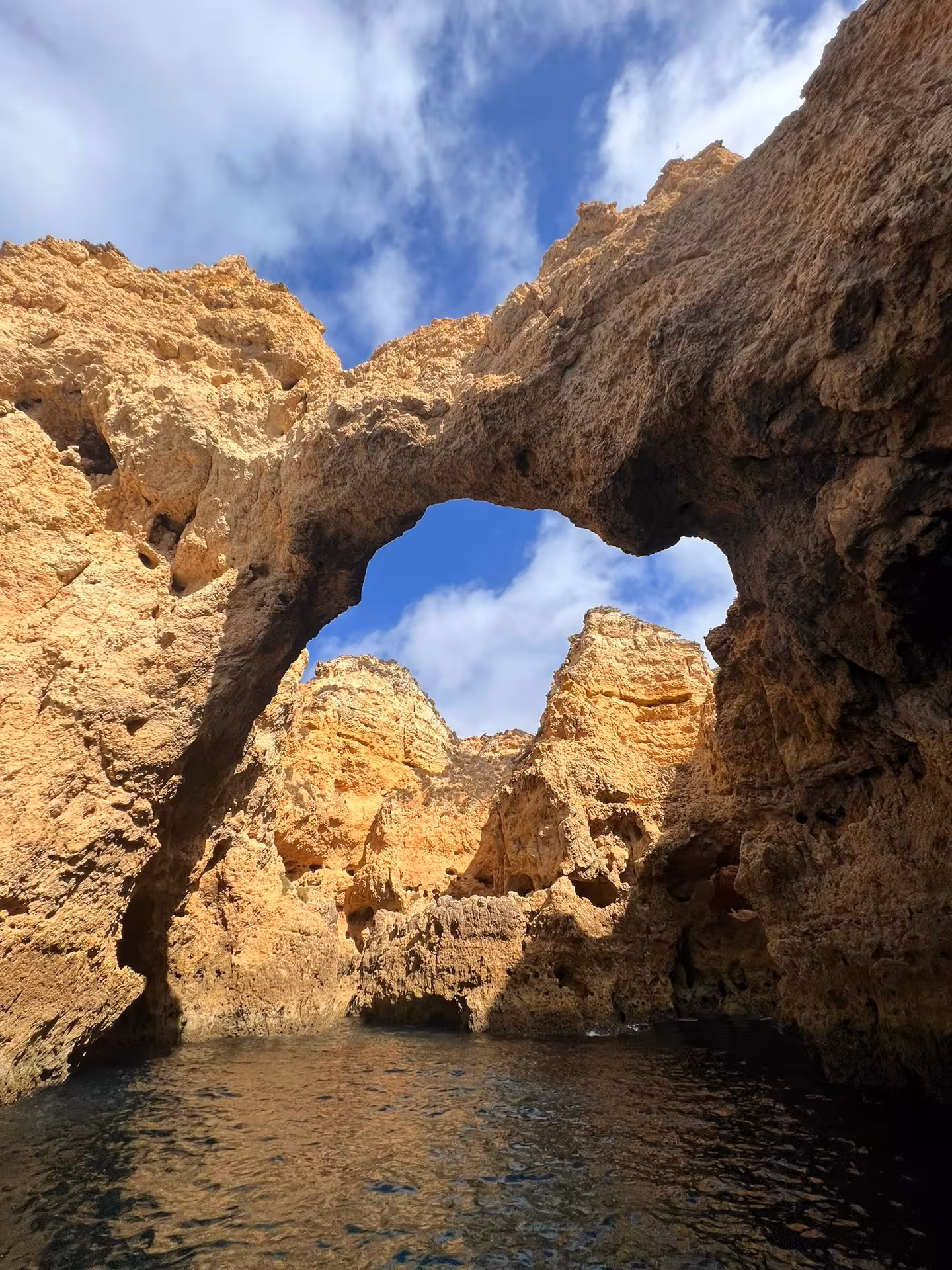 Boat tour view of Ponta da Piedade sea cave arch in Lagos Algarve, golden cliffs rising over calm Atlantic waters