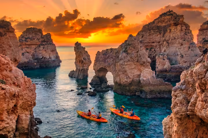 Kayakers paddling through stunning Ponta da Piedade sea caves and rock arches at dramatic sunset in Lagos Portugal